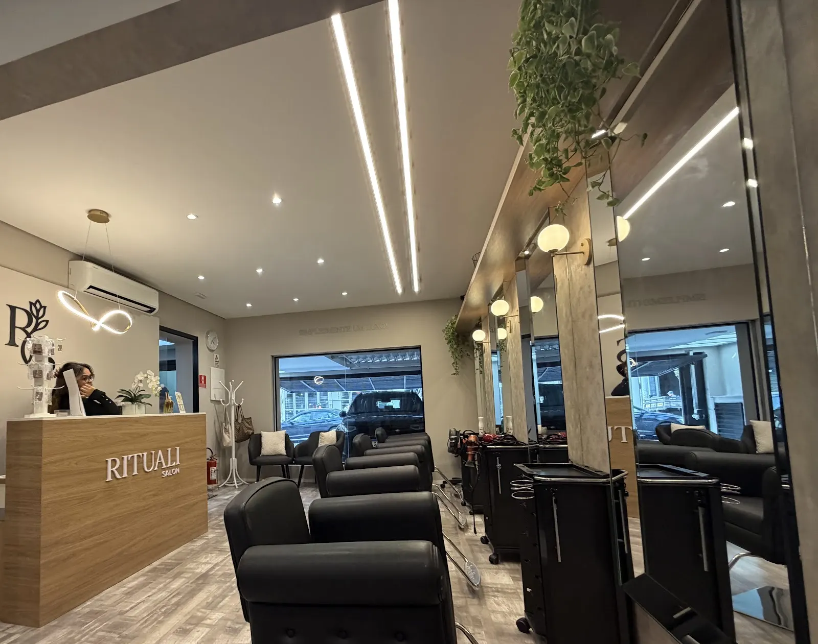 Recepção do Rituali Salon com balcão de madeira, linhas de luz no teto e poltronas pretas ao fundo