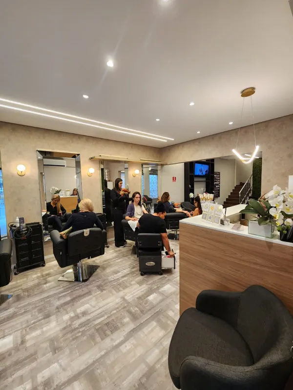 Salão principal com poltronas, espelhos e clientes sendo atendidas
